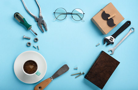 Fathers day holiday card concept with craft gift box, black mustache, cup of coffee, tools, book and glasses on blue background, top view, copy space.の写真素材
