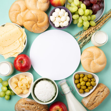 Happy Shavuot holiday card. Jewish religious holiday concept. Dairy products, fruits, cheese, bread, milk bottle, cottage cheese, wheat on blue mint background. Top view, copy space.の写真素材