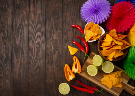 Cinco de Mayo (Fifth of May) celebration concept. Mexican background fiesta with Traditional Mexican nachos chips, red chili peppers, green lime on dark wooden background. Top view, copy space.の写真素材