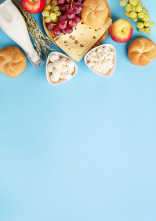 Happy Shavuot festive card, Jewish religious holiday concept. Dairy products, fruits, cheese, bread, milk bottle on blue background. Flat lay, top view, copy space.の写真素材