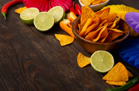 Cinco de Mayo (Fifth of May) celebration concept. Mexican background fiesta with Traditional Mexican nachos chips, red chili peppers, green lime on dark wooden background. Top view, copy space.の写真素材