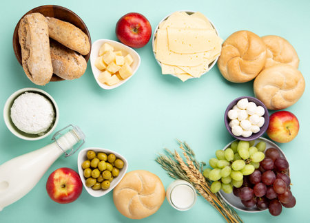 Happy Shavuot holiday card. Jewish religious holiday concept. Dairy products, fruits, cheese, bread, milk bottle, cottage cheese, wheat on blue mint background. Top view, copy space.の写真素材