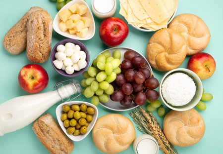 Happy Shavuot holiday card. Jewish religious holiday concept. Dairy products, fruits, cheese, bread, milk bottle, cottage cheese, wheat on blue mint background. Top view, copy space.の写真素材
