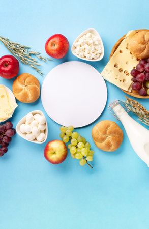 Happy Shavuot festive card, Jewish religious holiday concept. Dairy products, fruits, cheese, bread, milk bottle on blue background. Flat lay, top view, copy space.の写真素材