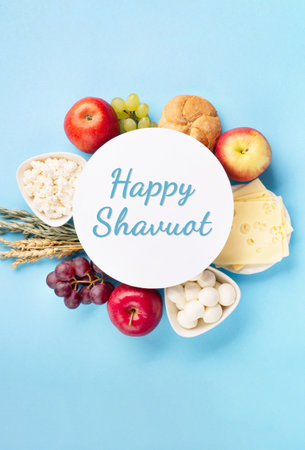 Happy Shavuot festive card, Jewish religious holiday concept. Dairy products, fruits, cheese, bread, milk bottle on blue background. Flat lay, top view, copy space.の写真素材