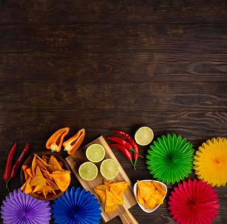 Cinco de Mayo (Fifth of May) celebration concept. Mexican background fiesta with Traditional Mexican nachos chips, red chili peppers, green lime on dark wooden background. Top view, copy space.の写真素材