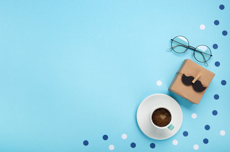 Fathers day holiday card concept with craft gift box, black mustache, cup of coffee and glasses on blue background, top view, copy space.の写真素材