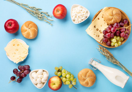 Happy Shavuot festive card, Jewish religious holiday concept. Dairy products, fruits, cheese, bread, milk bottle on blue background. Flat lay, top view, copy space.の写真素材