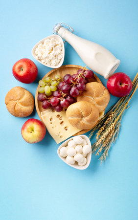 Happy Shavuot festive card, Jewish religious holiday concept. Dairy products, fruits, cheese, bread, milk bottle on blue background. Flat lay, top view, copy space.の写真素材