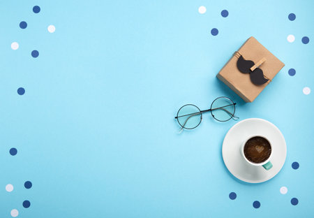 Fathers day holiday card concept with craft gift box, black mustache, cup of coffee and glasses on blue background, top view, copy space.の写真素材