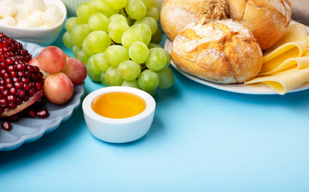 Happy Shavuot holiday card. Jewish religious holiday concept. Dairy products, grapes, cheese, bread, milk, cottage cheese, wheat, honey on blue background, copy space.の写真素材