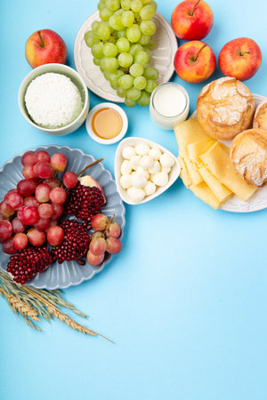 Happy Shavuot holiday card. Jewish religious holiday concept. Dairy products, grapes, cheese, bread, milk, cottage cheese, wheat, honey on blue background. Top view, copy space.の写真素材