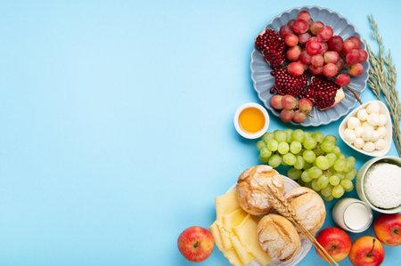 Happy Shavuot holiday card. Jewish religious holiday concept. Dairy products, grapes, cheese, bread, milk, cottage cheese, wheat, honey on blue background. Top view, copy space.の写真素材