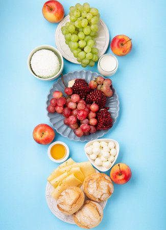 Happy Shavuot holiday card. Jewish religious holiday concept. Dairy products, grapes, cheese, bread, milk, cottage cheese, wheat, honey on blue background. Top view, copy space.の写真素材