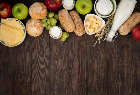 Happy Shavuot holiday card. Jewish religious holiday concept. Dairy products, fruits, cheese, bread, milk bottle, cottage cheese, wheat on dark wooden background. Top view, copy space.の写真素材