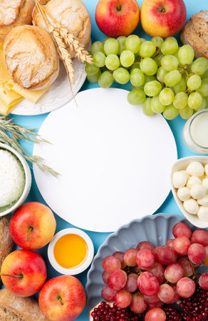 Happy Shavuot holiday card. Jewish religious holiday concept. Dairy products, grapes, cheese, bread, milk, cottage cheese, wheat, honey on blue background. Top view, copy space.の写真素材