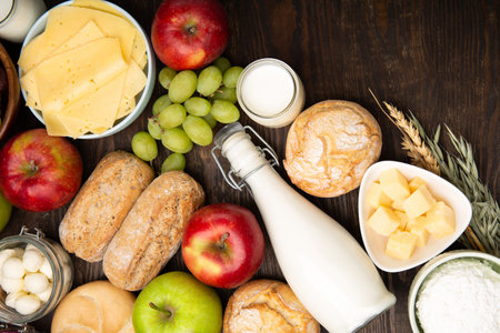 Happy Shavuot holiday card. Jewish religious holiday concept. Dairy products, fruits, cheese, bread, milk bottle, cottage cheese, wheat on dark wooden background. Top view, copy space.の写真素材