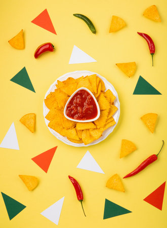 Mexican fiesta background with Traditional Mexican nachos chips, chilli peppers and tomato salsa sauce on yellow background. Cinco de Mayo (Fifth of May) celebration concept. Top view, copy space.の写真素材