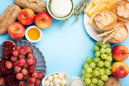 Happy Shavuot holiday card. Jewish religious holiday concept. Dairy products, grapes, cheese, bread, milk, cottage cheese, wheat, honey on blue background. Top view, copy space.の写真素材
