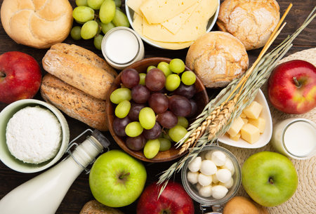 Happy Shavuot holiday card. Jewish religious holiday concept. Dairy products, fruits, cheese, bread, milk bottle, cottage cheese, wheat on dark wooden background, Top view.の写真素材
