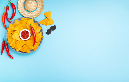 Mexican fiesta background with Traditional Mexican nachos chips, chilli peppers and tomato salsa sauce on blue table. Cinco de Mayo (Fifth of May) celebration concept. Top view, copy space.の写真素材