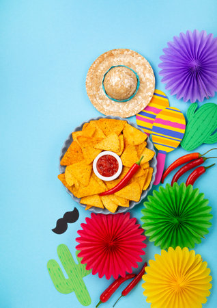 Mexican fiesta background with Traditional Mexican nachos chips, chilli peppers and tomato salsa sauce on blue table. Cinco de Mayo (Fifth of May) celebration concept. Top view, copy space.の写真素材