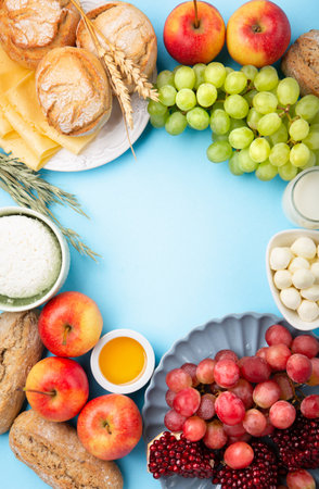 Happy Shavuot holiday card. Jewish religious holiday concept. Dairy products, grapes, cheese, bread, milk, cottage cheese, wheat, honey on blue background. Top view, copy space.の写真素材