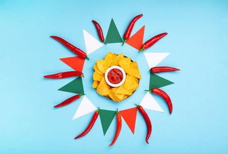 Mexican fiesta background with Traditional Mexican nachos chips, chilli peppers and tomato salsa sauce on blue table. Cinco de Mayo (Fifth of May) celebration concept. Top view, copy space.の写真素材