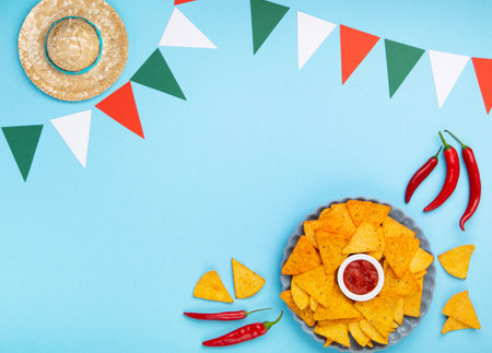 Mexican fiesta background with Traditional Mexican nachos chips, chilli peppers and tomato salsa sauce on blue table. Cinco de Mayo (Fifth of May) celebration concept. Top view, copy space.の写真素材
