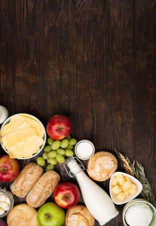 Happy Shavuot holiday card. Jewish religious holiday concept. Dairy products, fruits, cheese, bread, milk bottle, cottage cheese, wheat on dark wooden background. Top view, copy space.の写真素材