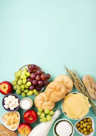 Happy Shavuot holiday card. Jewish religious holiday concept. Dairy products, fruits, cheese, bread, milk bottle, cottage cheese, wheat on blue mint background. Top view, copy space.の写真素材