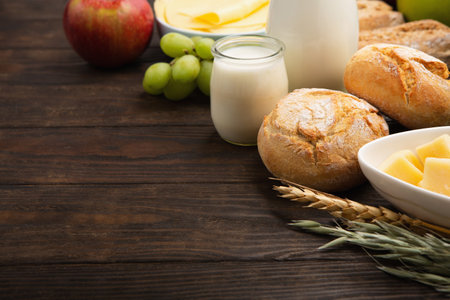 Happy Shavuot holiday card. Jewish religious holiday concept. Dairy products, fruits, cheese, bread, milk bottle, cottage cheese, wheat on dark wooden background, copy space.の写真素材