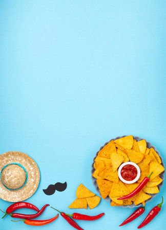 Mexican fiesta background with Traditional Mexican nachos chips, chilli peppers and tomato salsa sauce on blue table. Cinco de Mayo (Fifth of May) celebration concept. Top view, copy space.の写真素材