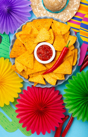 Mexican fiesta background with Traditional Mexican nachos chips, chilli peppers and tomato salsa sauce on blue table. Cinco de Mayo (Fifth of May) celebration concept. Top view, copy space.の写真素材