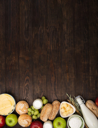 Happy Shavuot holiday card. Jewish religious holiday concept. Dairy products, fruits, cheese, bread, milk bottle, cottage cheese, wheat on dark wooden background. Top view, copy space.の写真素材