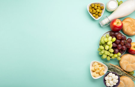 Happy Shavuot holiday card. Jewish religious holiday concept. Dairy products, fruits, cheese, bread, milk bottle, cottage cheese, wheat on blue mint background. Top view, copy space.の写真素材