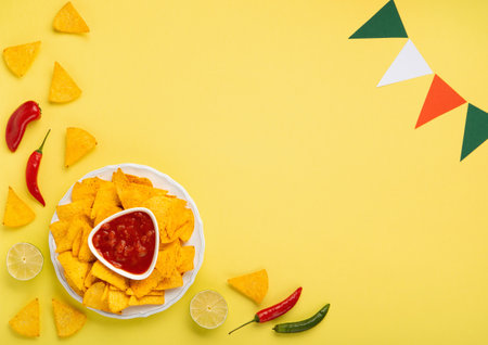 Mexican fiesta background with Traditional Mexican nachos chips, chilli peppers and tomato salsa sauce on yellow background. Cinco de Mayo (Fifth of May) celebration concept. Top view, copy space.の写真素材