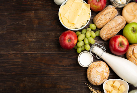 Happy Shavuot holiday card. Jewish religious holiday concept. Dairy products, fruits, cheese, bread, milk bottle, cottage cheese, wheat on dark wooden background. Top view, copy space.の写真素材