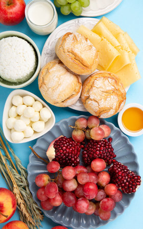 Happy Shavuot holiday card. Jewish religious holiday concept. Dairy products, grapes, cheese, bread, milk, cottage cheese, wheat, honey on blue background. top view.の写真素材