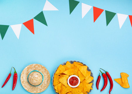 Mexican fiesta background with Traditional Mexican nachos chips, chilli peppers and tomato salsa sauce on blue table. Cinco de Mayo (Fifth of May) celebration concept. Top view, copy space.の写真素材