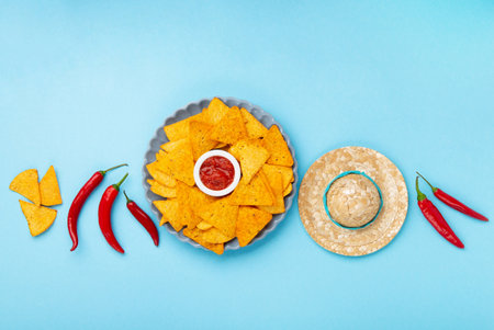 Mexican fiesta background with Traditional Mexican nachos chips, chilli peppers and tomato salsa sauce on blue table. Cinco de Mayo (Fifth of May) celebration concept. Top view, copy space.の写真素材
