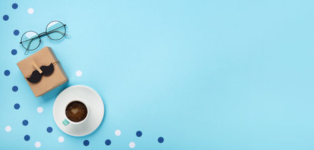 Fathers day holiday card concept with craft gift box, black mustache, cup of coffee and glasses on blue background, top view, copy space.の写真素材