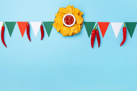 Mexican fiesta background with Traditional Mexican nachos chips, chilli peppers and tomato salsa sauce on blue table. Cinco de Mayo (Fifth of May) celebration concept. Top view, copy space.の写真素材