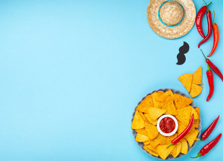 Mexican fiesta background with Traditional Mexican nachos chips, chilli peppers and tomato salsa sauce on blue table. Cinco de Mayo (Fifth of May) celebration concept. Top view, copy space.の写真素材