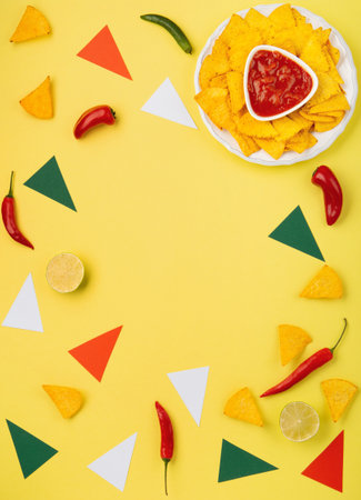 Mexican fiesta background with Traditional Mexican nachos chips, chilli peppers and tomato salsa sauce on yellow background. Cinco de Mayo (Fifth of May) celebration concept. Top view, copy space.の写真素材