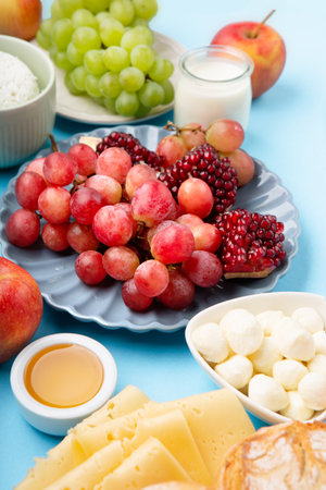Happy Shavuot holiday card. Jewish religious holiday concept. Dairy products, grapes, cheese, bread, milk, cottage cheese, wheat, honey on blue background. Top view, copy space.の写真素材