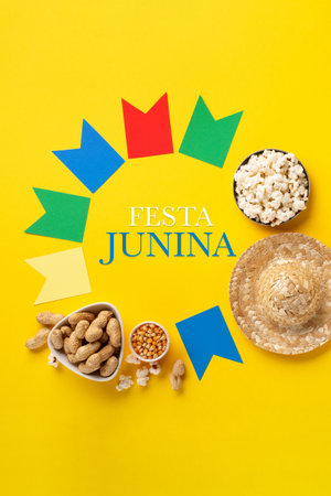Carnival Brazilian Festa Junina Summer Festival concept. Brazilian straw hat, popcorn, peanuts and colorful flags on yellow background, top view. Design for Greeting Card, Invitation or Holiday Posterの写真素材