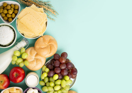 Happy Shavuot holiday card. Jewish religious holiday concept. Dairy products, fruits, cheese, bread, milk bottle, cottage cheese, wheat on blue mint background. Top view, copy space.の写真素材