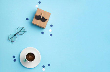 Fathers day holiday card concept with craft gift box, black mustache, cup of coffee and glasses on blue background, top view, copy space.の写真素材