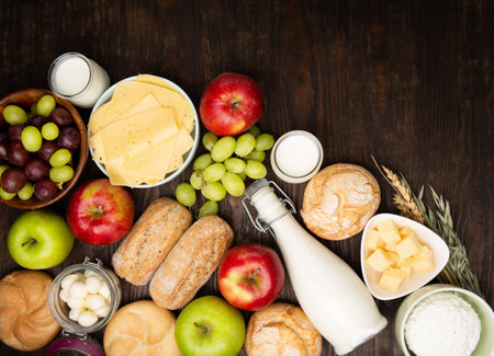 Happy Shavuot holiday card. Jewish religious holiday concept. Dairy products, fruits, cheese, bread, milk bottle, cottage cheese, wheat on dark wooden background. Top view, copy space.の写真素材